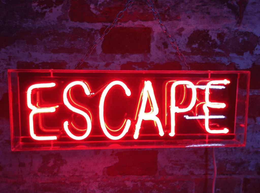 Lit-up neon 'escape' sign on brick wall.